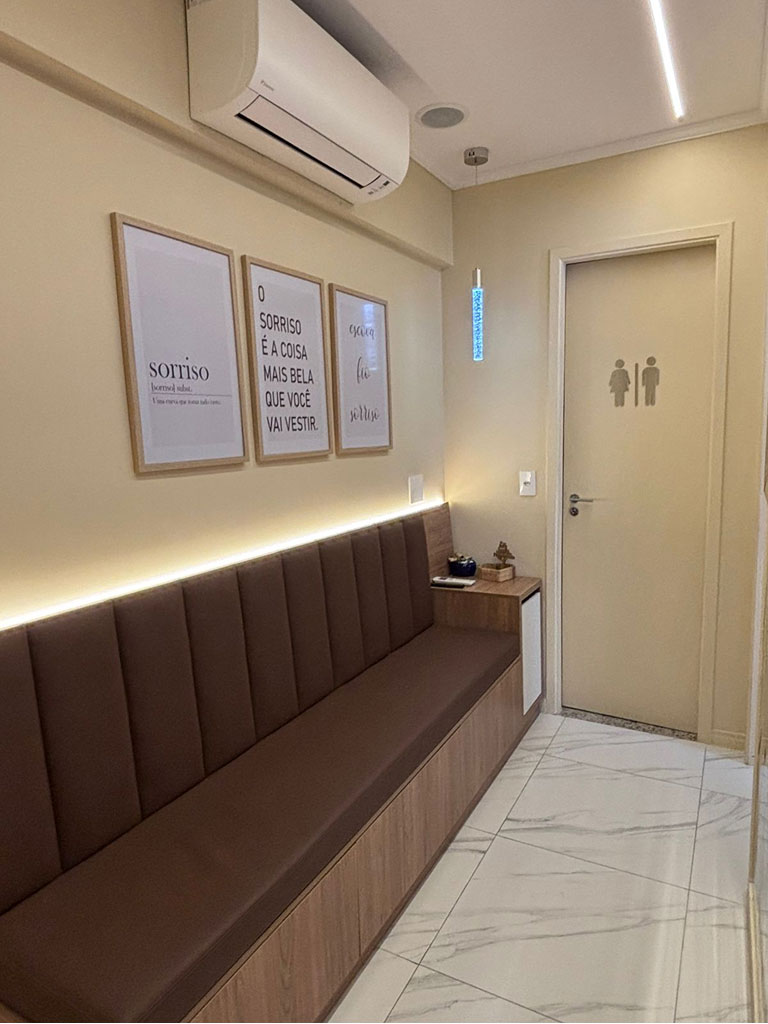 Recepção do consultório na Barra Funda, com banco estofado, iluminação indireta e quadros na parede